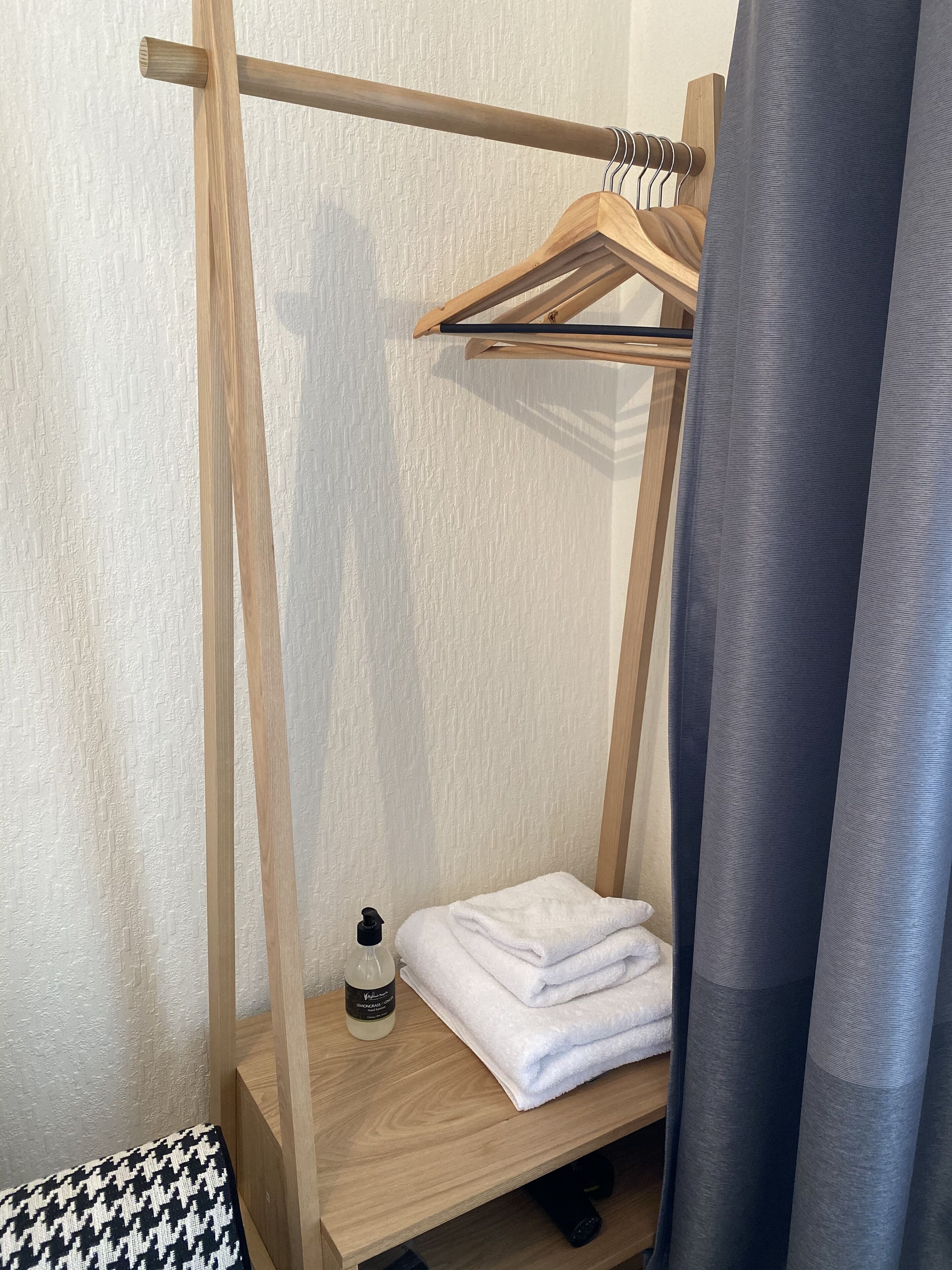 A wooden shelf with a towel and a bottle, a wooden hanger rack, and a grey curtain.