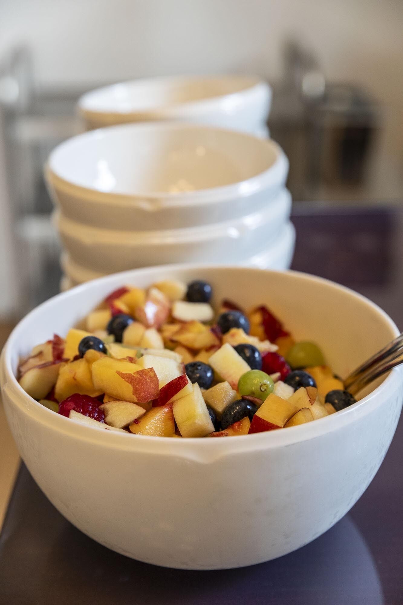 A bowl of fruit salad with various fruits and a spoon.