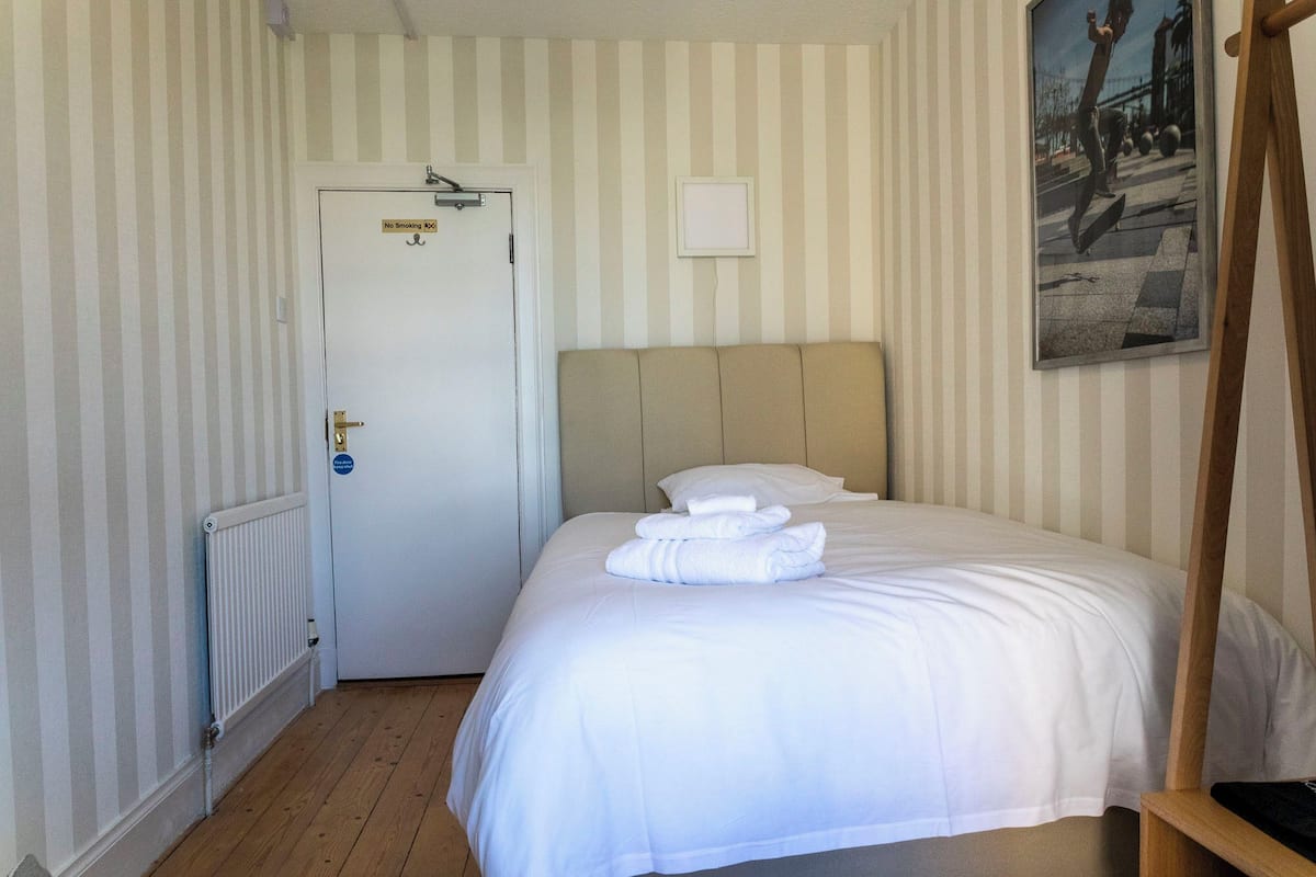 Una camera d'hotel con un letto, un termosifone, una porta con il cartello 'No Smoking' e un quadro appeso al muro.