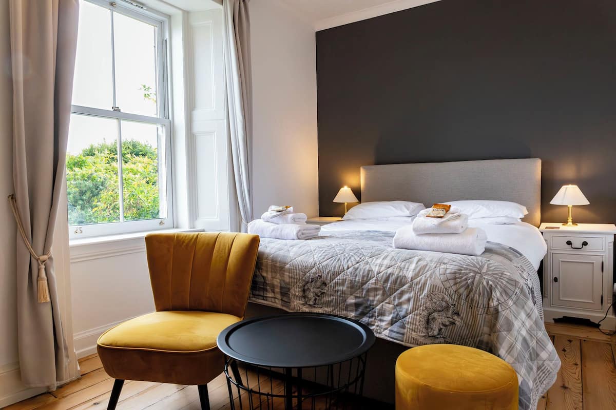 Una camera d'hotel con un letto, due abat-jour, una sedia, un tavolino rotondo e una finestra con tende.