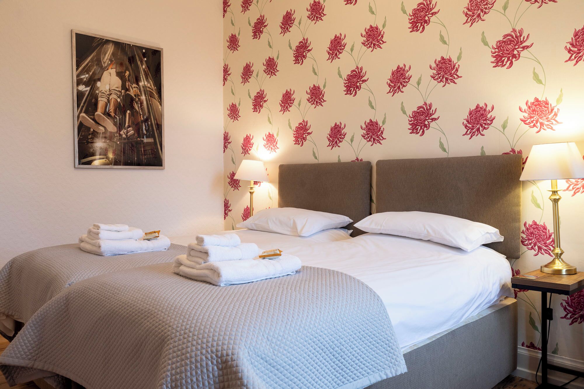 Una habitación de hotel con una cama, dos mesitas de noche y un papel tapiz floral.