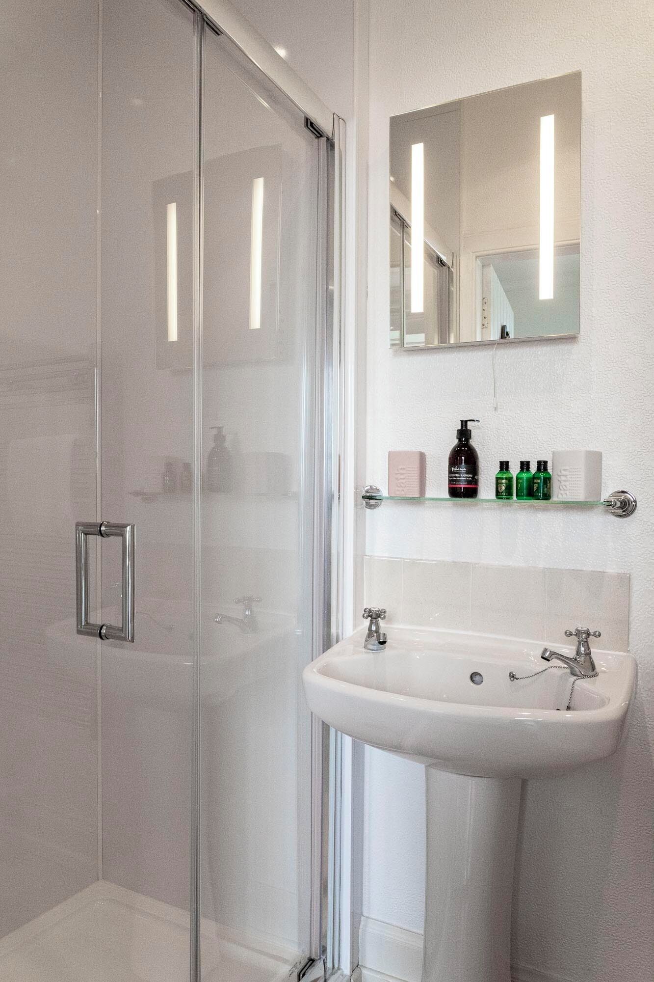A modern bathroom with a glass shower enclosure, a white sink with a single faucet, and a mirror above the sink.