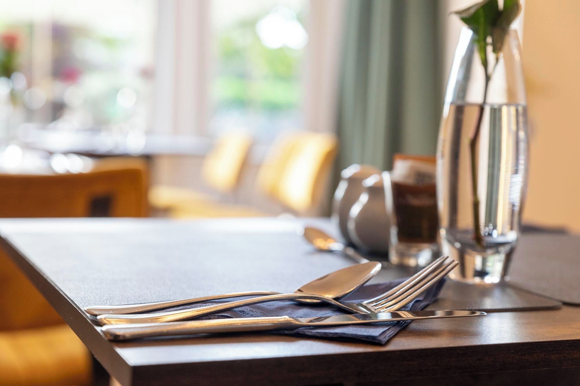 Une table à manger élégamment dressée, avec des couverts et un vase de fleurs.