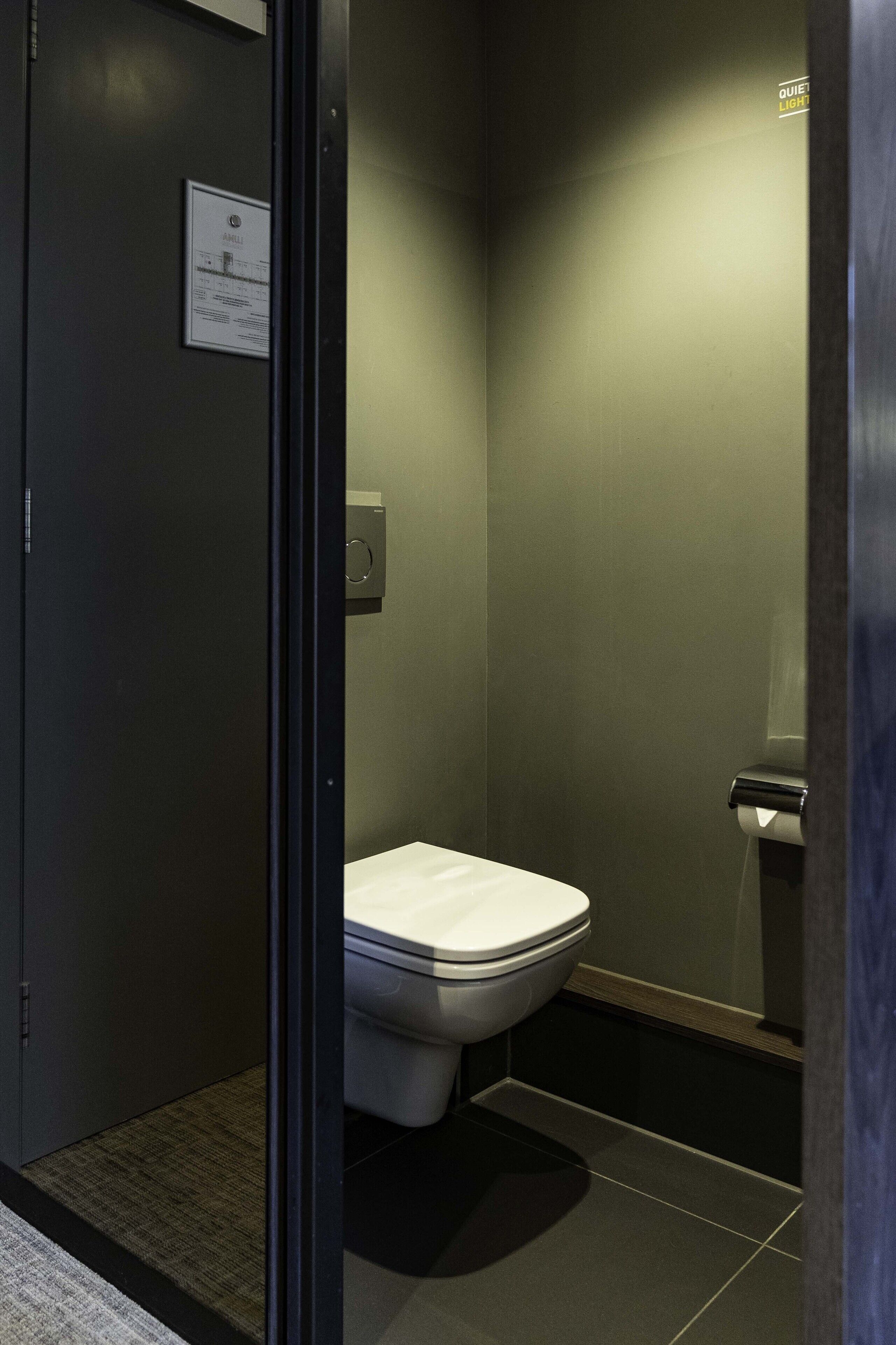 Un baño pequeño y tenuemente iluminado, con un inodoro blanco, un dispensador de toallas y un cartel en la pared.