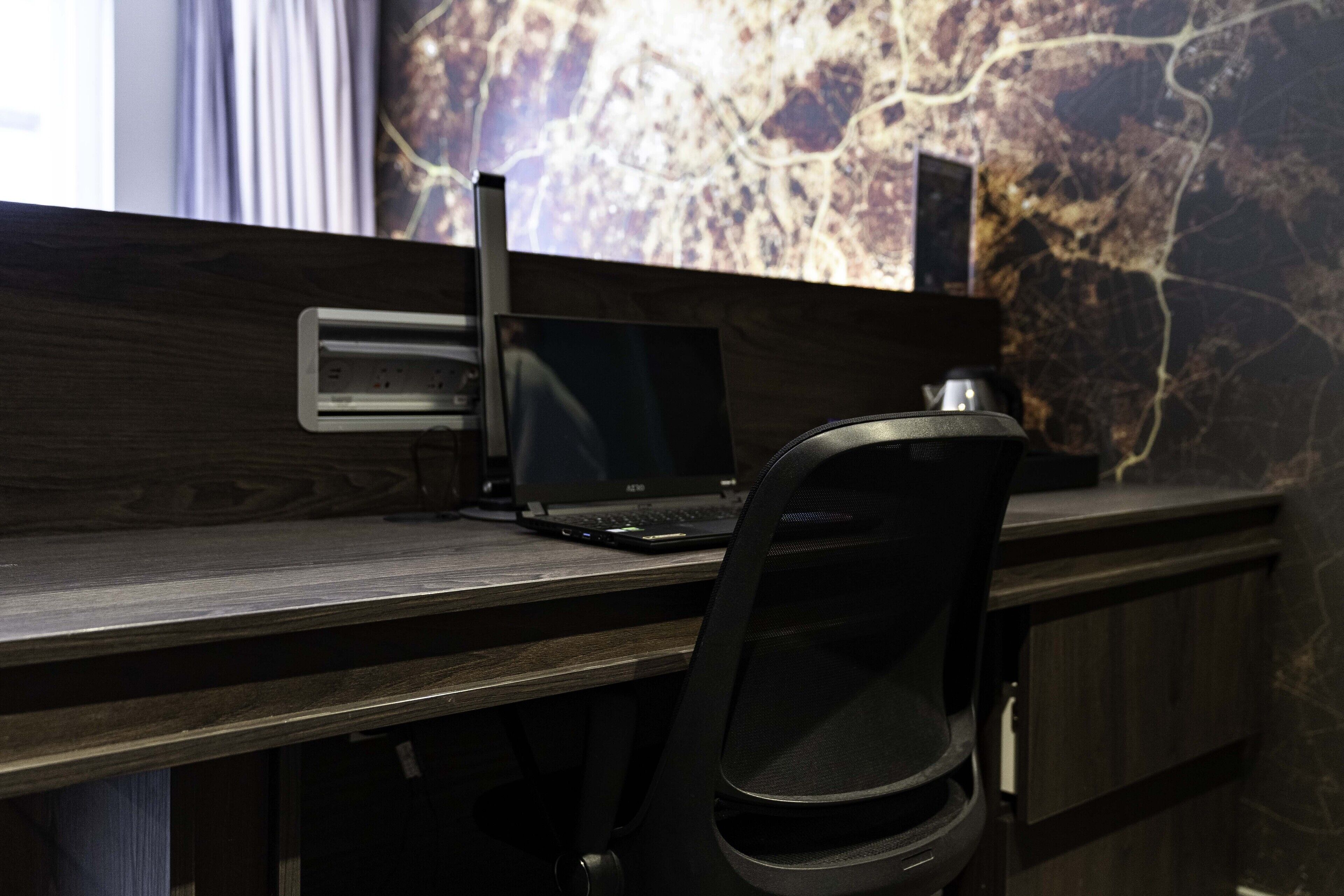 A modern office desk with a laptop, a chair, and a wall-mounted shelf.