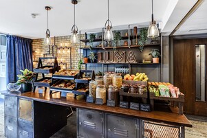 A breakfast bar with various food items, a sign reading 'LUMA', and a brick wall with shelves.