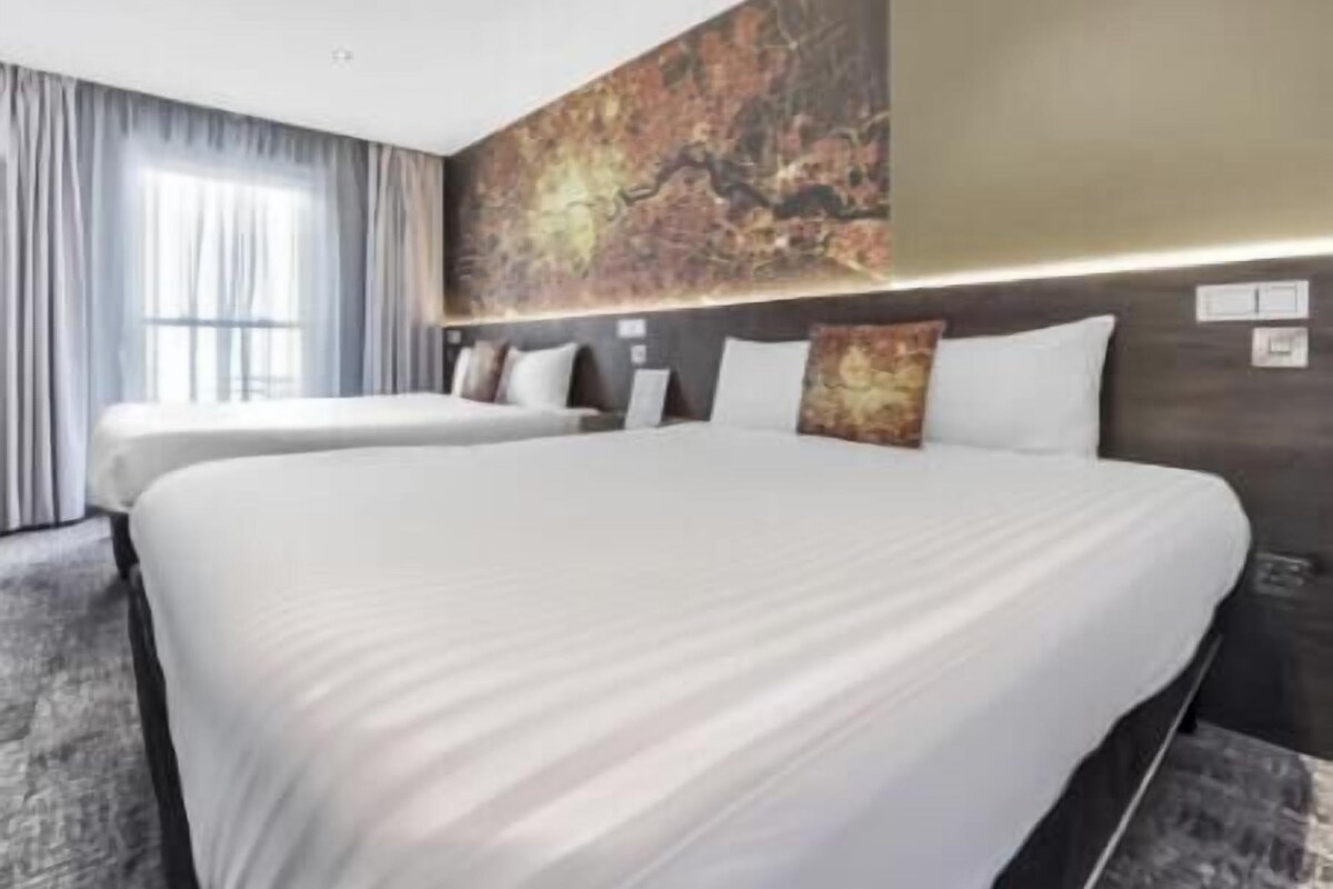 A hotel room with two beds, a large abstract wall art, and a modern design.