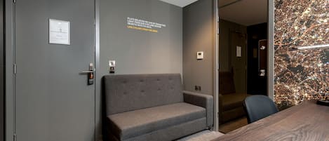 A modern hotel room with a grey sofa, a wooden table, and a cityscape wall art.