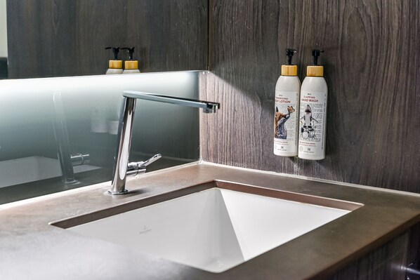 A bathroom with a modern sink, a mirror, and two hand wash bottles.