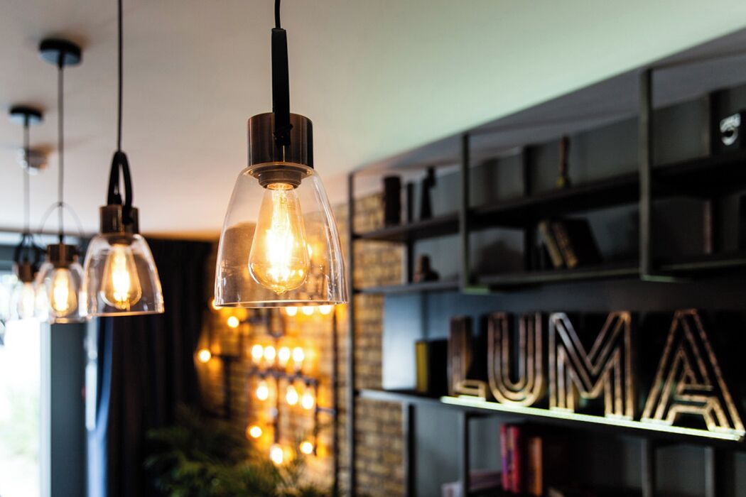 A modern interior with pendant lights, a brick wall, and a shelf with the word 'LUMA' illuminated.