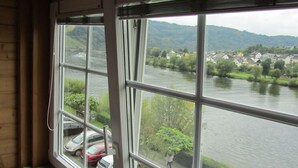 Blick aus einem Fenster auf einen Fluss mit parkenden Autos und einer Stadt im Hintergrund.