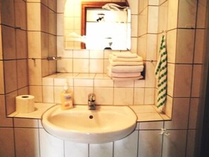 A bathroom with a sink, toilet paper, and a stack of towels. - Mosel Panorama (Zell (Mosel))