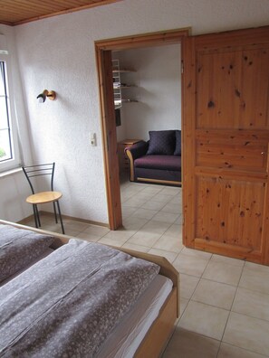 A bedroom with a bed, a chair, a wardrobe, and a view into another room with a sofa. - Mosel Panorama (Zell (Mosel))