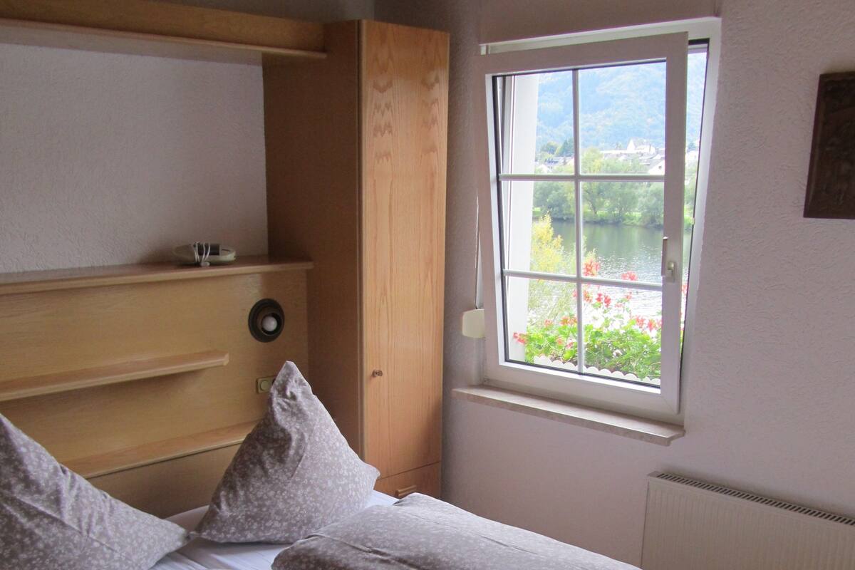 A bedroom with a wooden bed, a window with a view of greenery, and a radiator.
