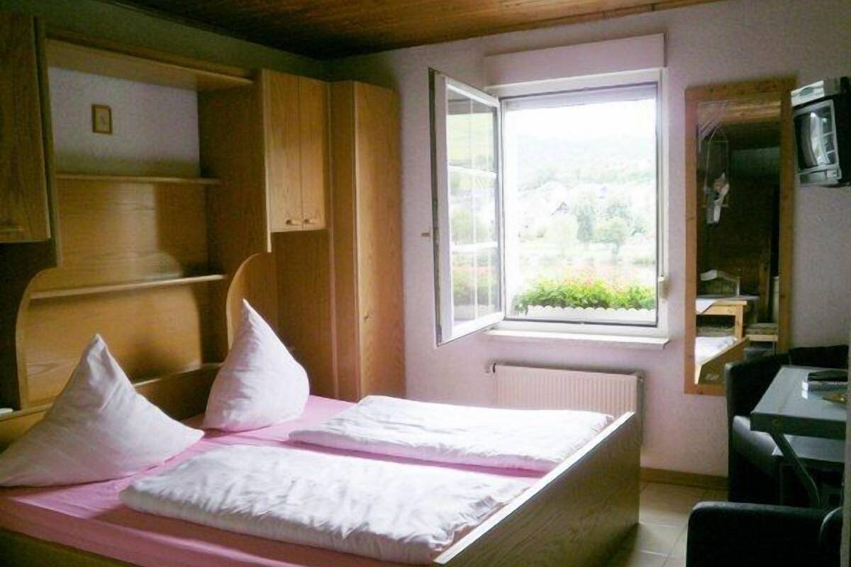 A bedroom with a bed, a window, and a desk.