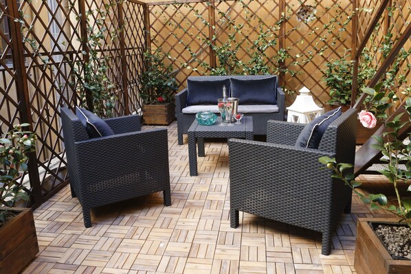 An outdoor patio with wicker furniture, a wooden floor, and a lattice fence. - Saint B Boutique Hotel STB (Rome)