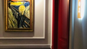 A hallway with a painting of a figure in a yellow dress, a red door, and a sign with numbers. - Saint B Boutique Hotel STB (Rome)