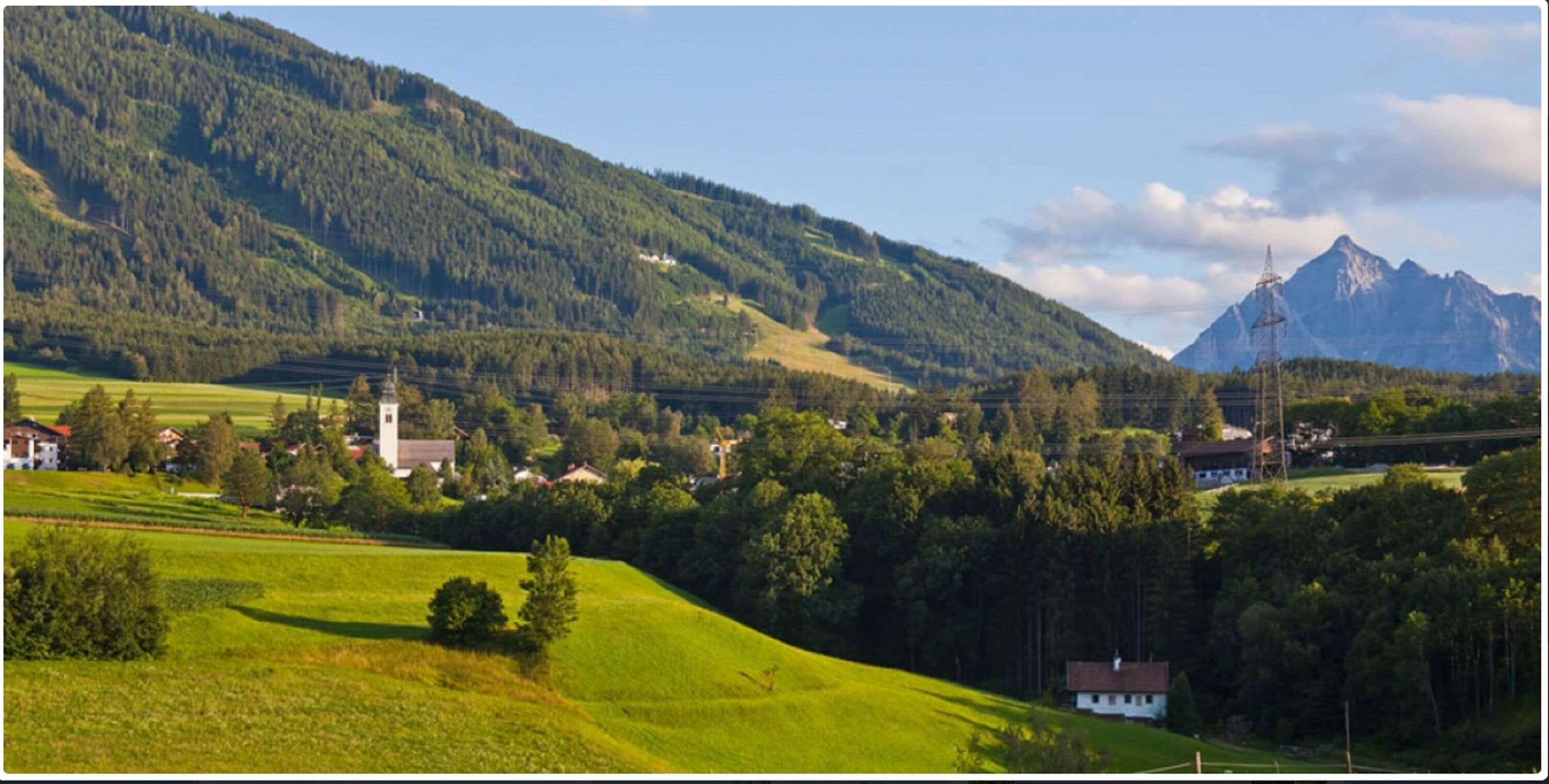 Un paysage rural avec une église, des maisons et une montagne en arrière-plan.