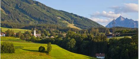 Un paysage rural avec une église, des maisons et une montagne en arrière-plan.