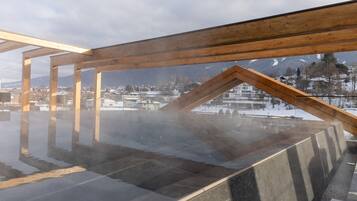 A sauna with a wooden roof structure and a view of a snowy landscape.