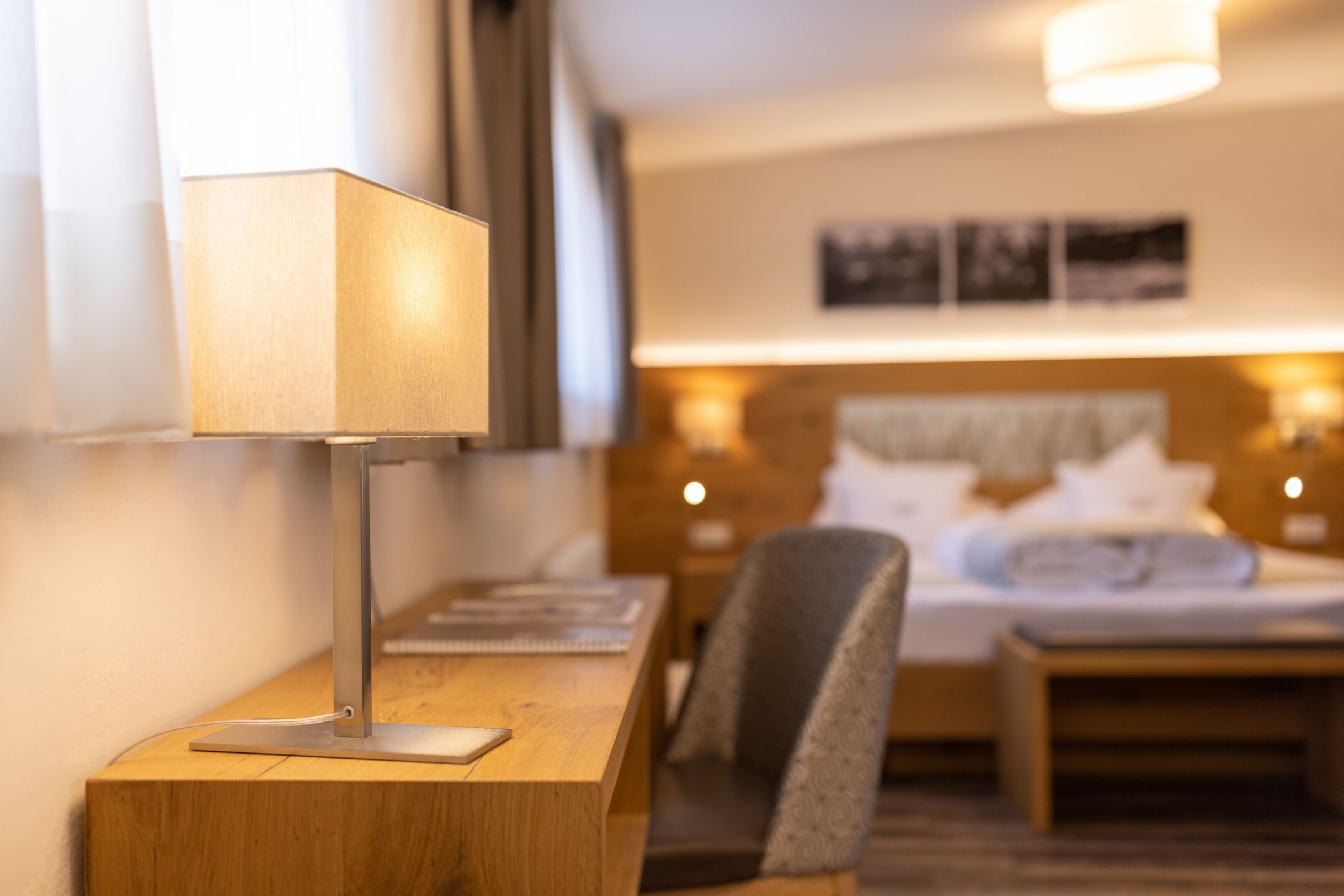 A hotel room with a desk, chair, bed, bedside lamps, and a wall-mounted picture.