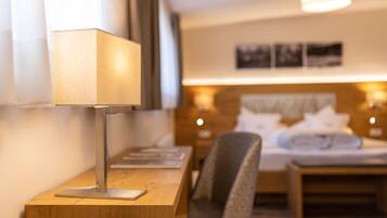 A hotel room with a desk, chair, bed, bedside lamps, and a wall-mounted picture.