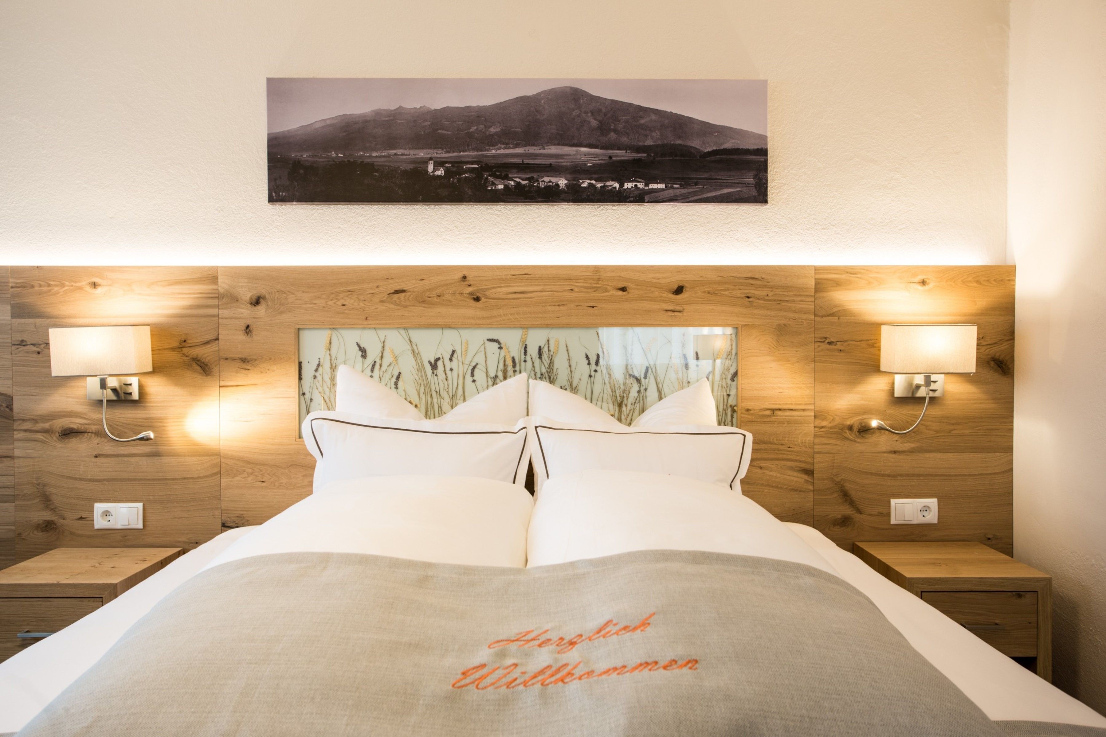 A neatly made bed with a headboard featuring a wooden panel design and two wall-mounted lamps.