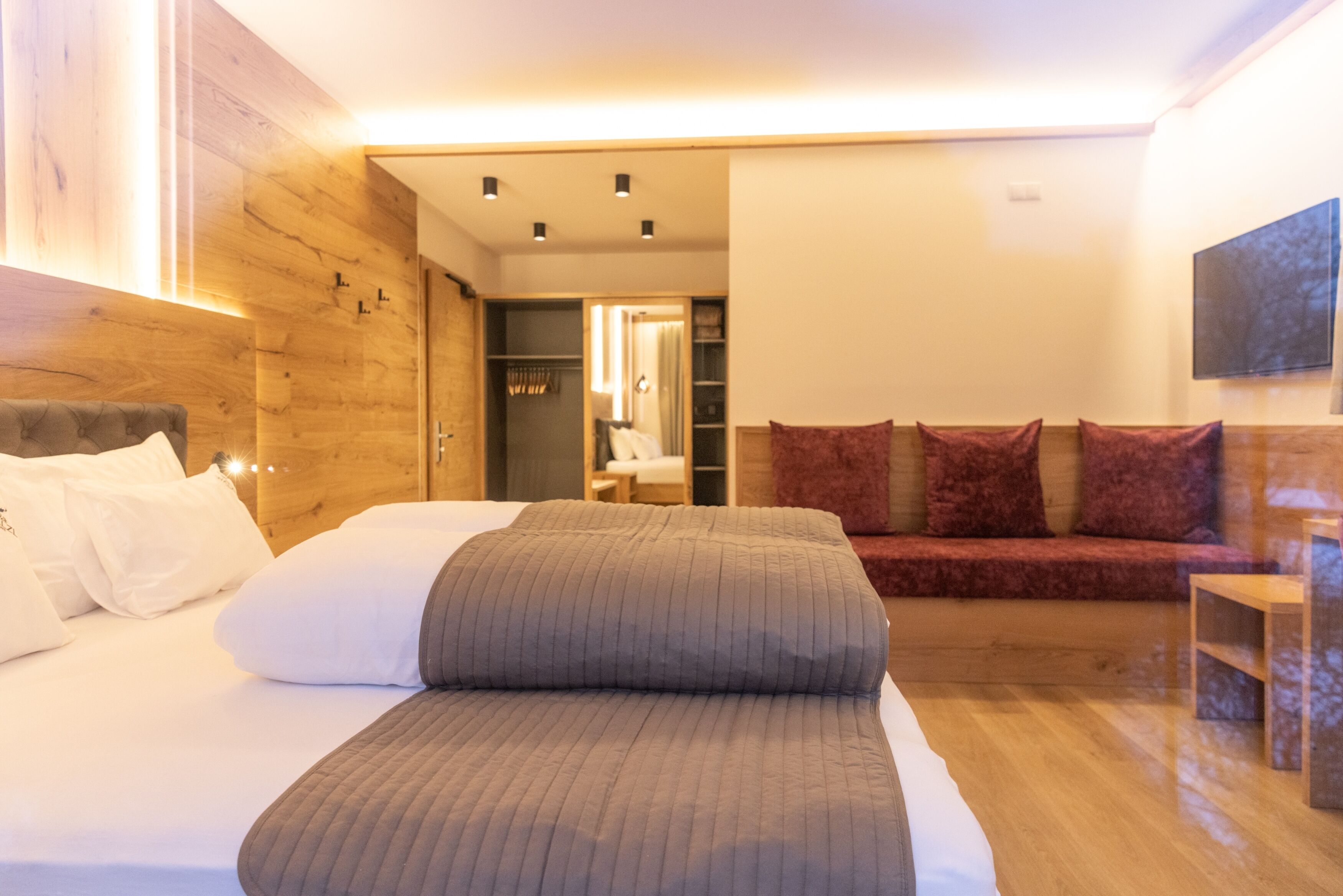 Un dormitorio moderno con una cama grande, un sofá rojo, paneles de madera y un televisor en la pared.