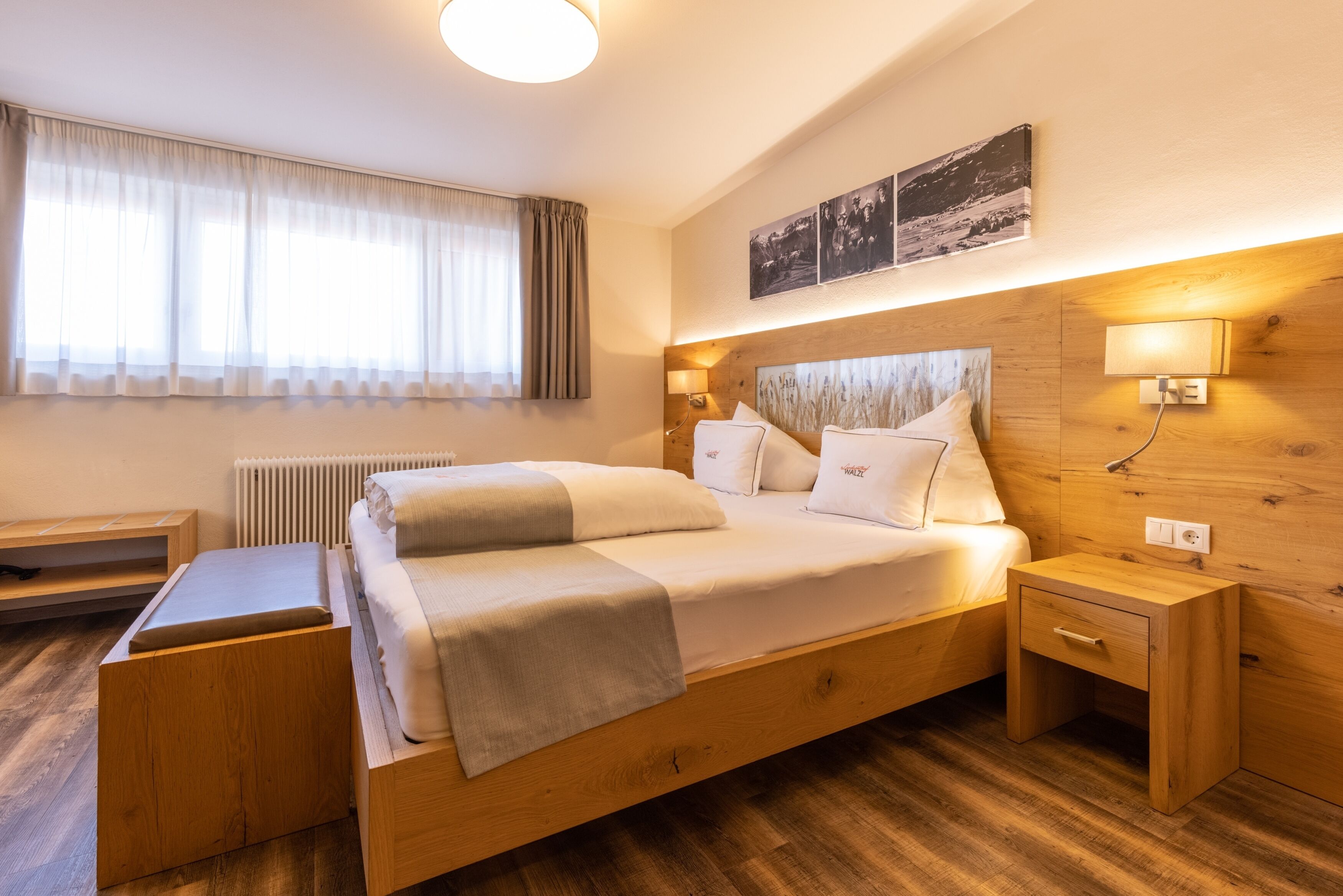 Une chambre d’hôtel moderne avec un lit en bois, des tables de chevet, un petit bureau et un radiateur.