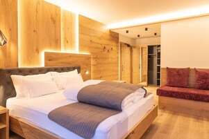 Um quarto moderno com cabeceira de madeira, uma cama grande com roupa de cama branca e cinza, e um sofá vermelho.