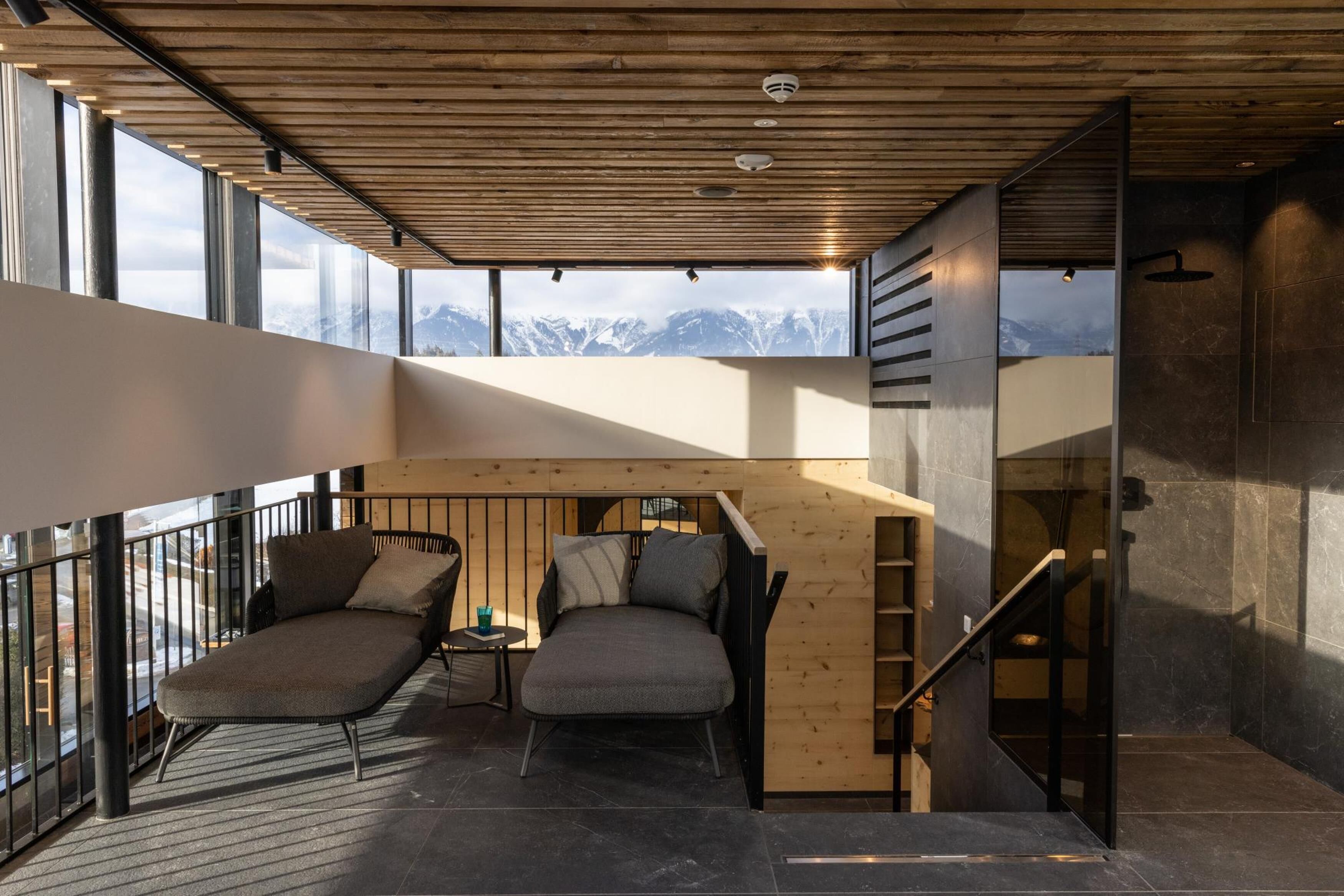 A modern interior with a wooden ceiling, large windows, a sofa, and a staircase.
