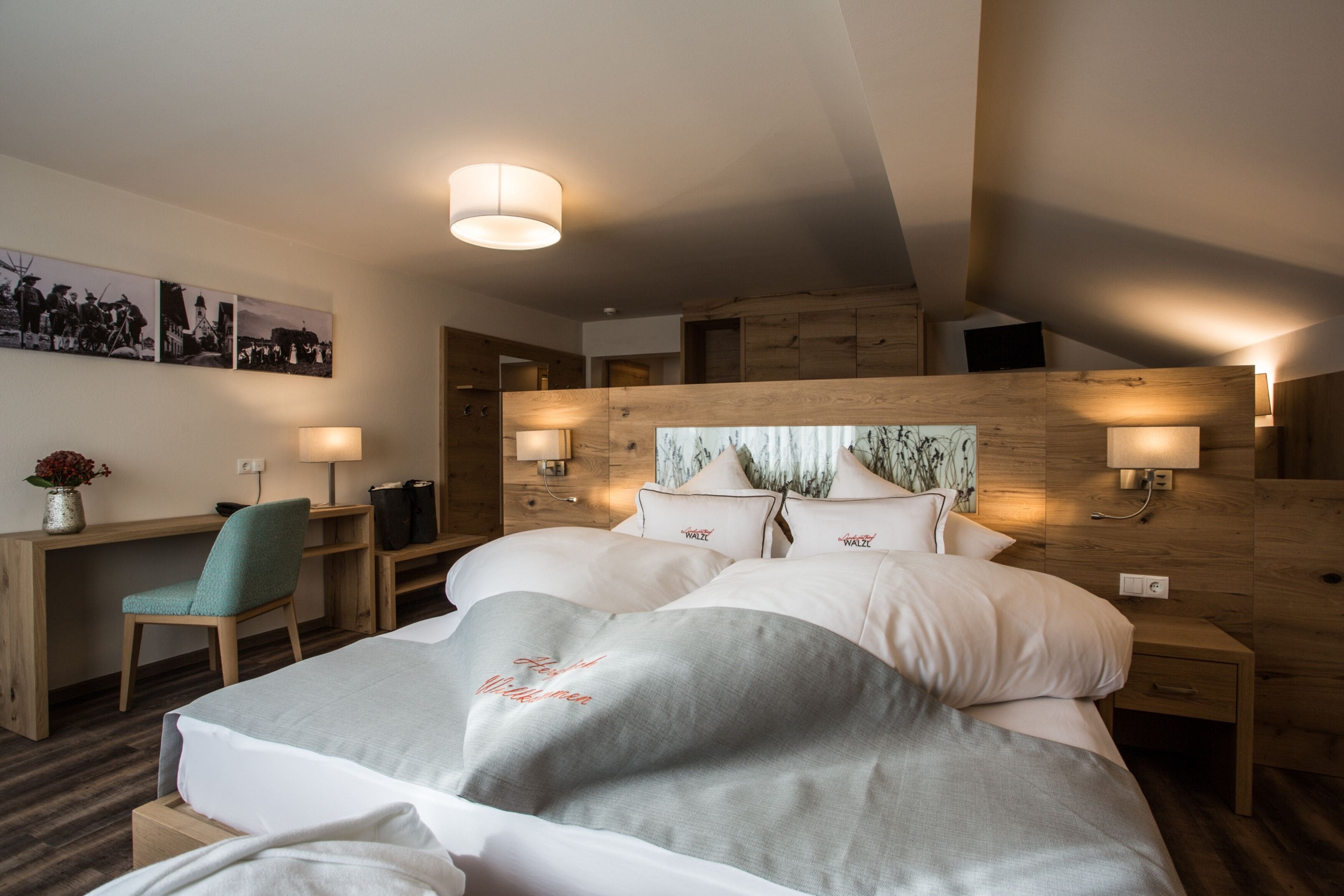 A hotel room with a large bed, wooden headboard, bedside lamps, a desk, and a chair.