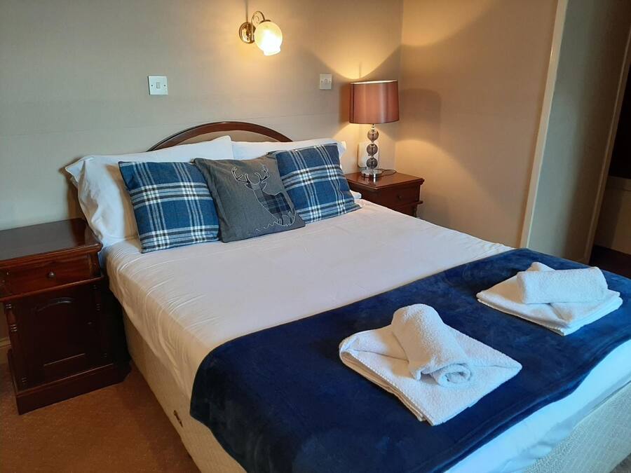 A neatly made bed with a blue blanket and two white towels, a wooden nightstand with a lamp, and a wall-mounted light fixture.