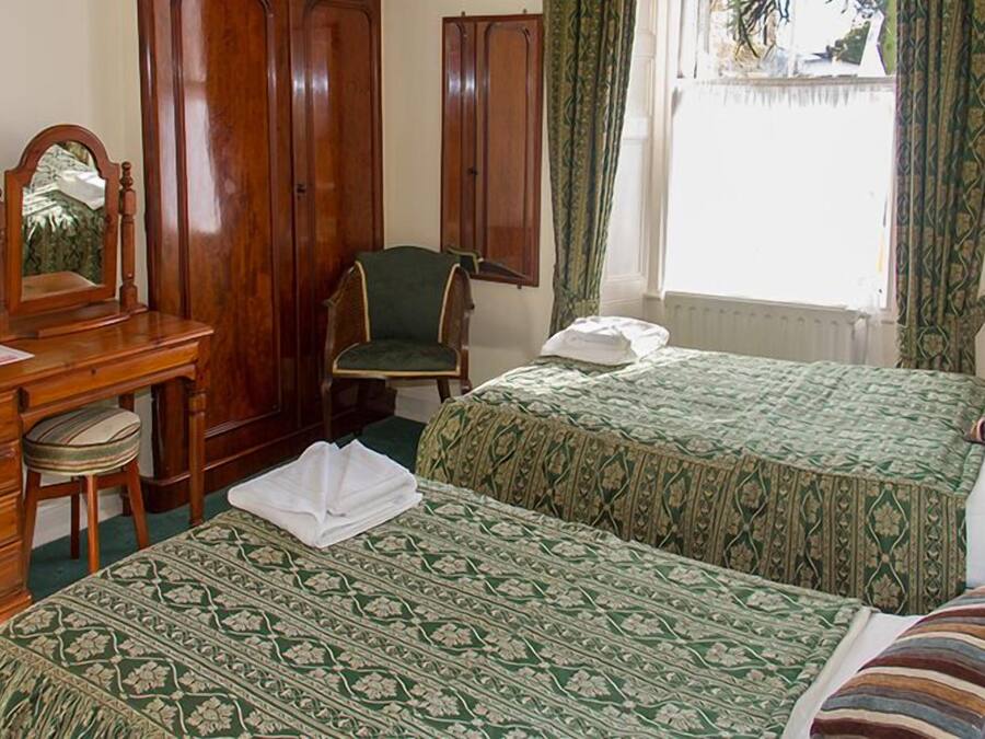 Una habitación con dos camas, un aparador de madera, una silla, un espejo y una ventana con cortinas.