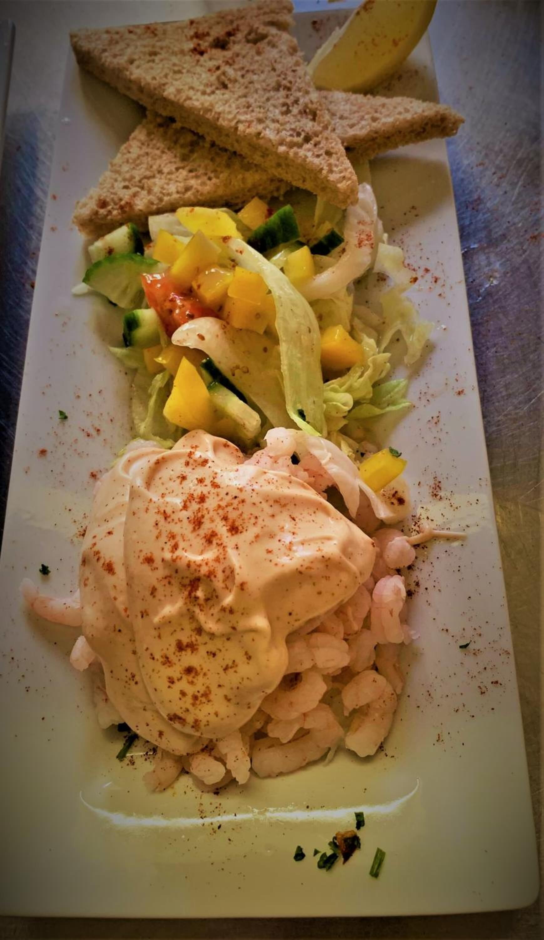 A plate with a salad, shrimp, and bread.
