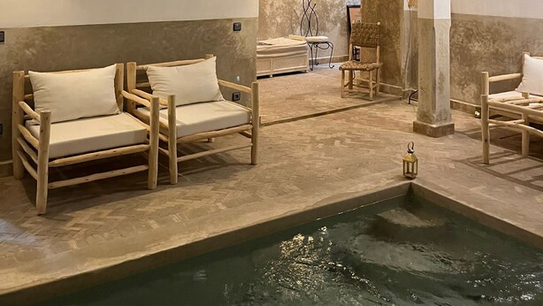 A spa area with wooden loungers, a small pool, and a stone wall. - RIAD NAFORA  (Marrakech)