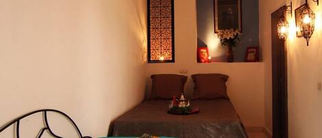 A small, cozy bedroom with a bed, pillows, a nightstand, and a decorative wall panel.