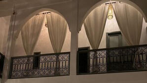 A spacious interior with high arched ceilings, a wooden sofa, a wicker chair, and a door with a metal gate. - RIAD NAFORA  (Marrakech)