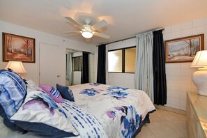 Ein Schlafzimmer mit einem Bett, einem Deckenventilator, einem Fenster mit Vorhängen und zwei Wandleuchten.