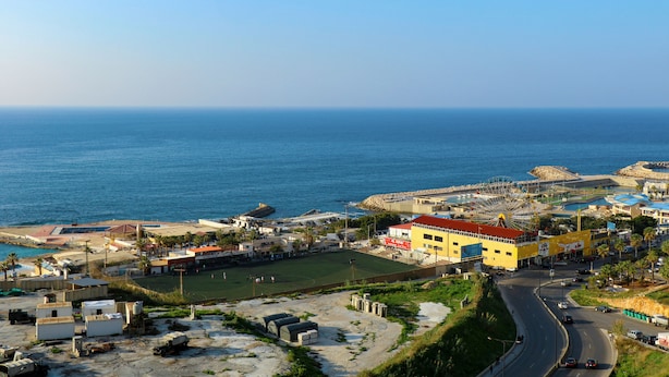A coastal town with a prominent yellow building, a road, and a beach area. - Grand Suites Hotel (Beirut)