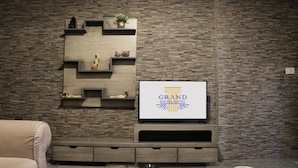 A modern living room with a stone-patterned wall, a mounted flat-screen TV, and a built-in entertainment unit. - Grand Suites Hotel (Beirut)
