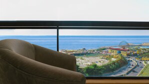 A room with a large window overlooking a coastal area, including a road and a Ferris wheel. - Grand Suites Hotel (Beirut)