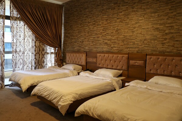 A hotel room with three beds, a brick wall, and a window with curtains.