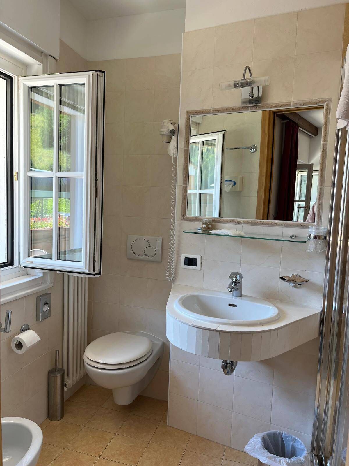 Un bagno con toilette, bidet, lavandino e una finestra che si affaccia sul verde.