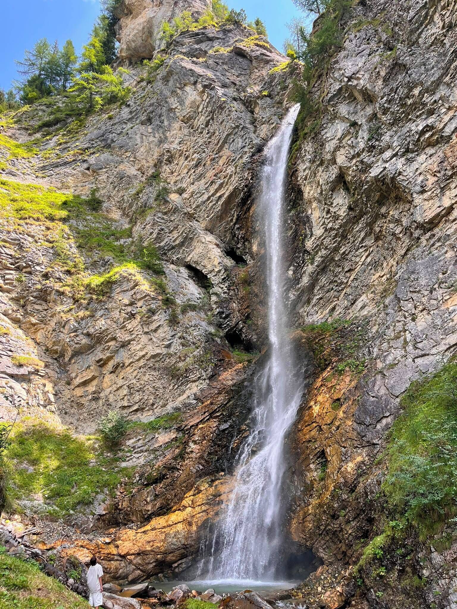 A waterfall cascading down a rocky cliff surrounded by greenery.