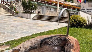 A stone fountain in a courtyard with a building featuring balconies and flower boxes in the background. - La Meridiana (Madesimo)