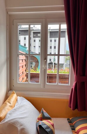 Quarto com cama, janela com cortinas e vista para edifícios e um jardim.