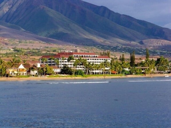A coastal hotel with multiple floors, a beach view, and a mountainous backdrop.