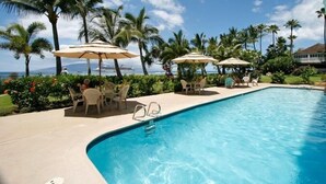 A swimming pool with lounge chairs and umbrellas, surrounded by palm trees and a view of the ocean. - Lahaina Shores #532 Studio Bedroom Condo by RedAwning (Lahaina)