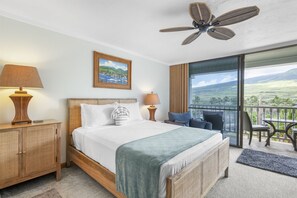 Ein Schlafzimmer mit Bett, Nachttischlampen, einem Weidenbeistelltisch, Blick ins Freie durch eine Schiebetür und Deckenventilator.